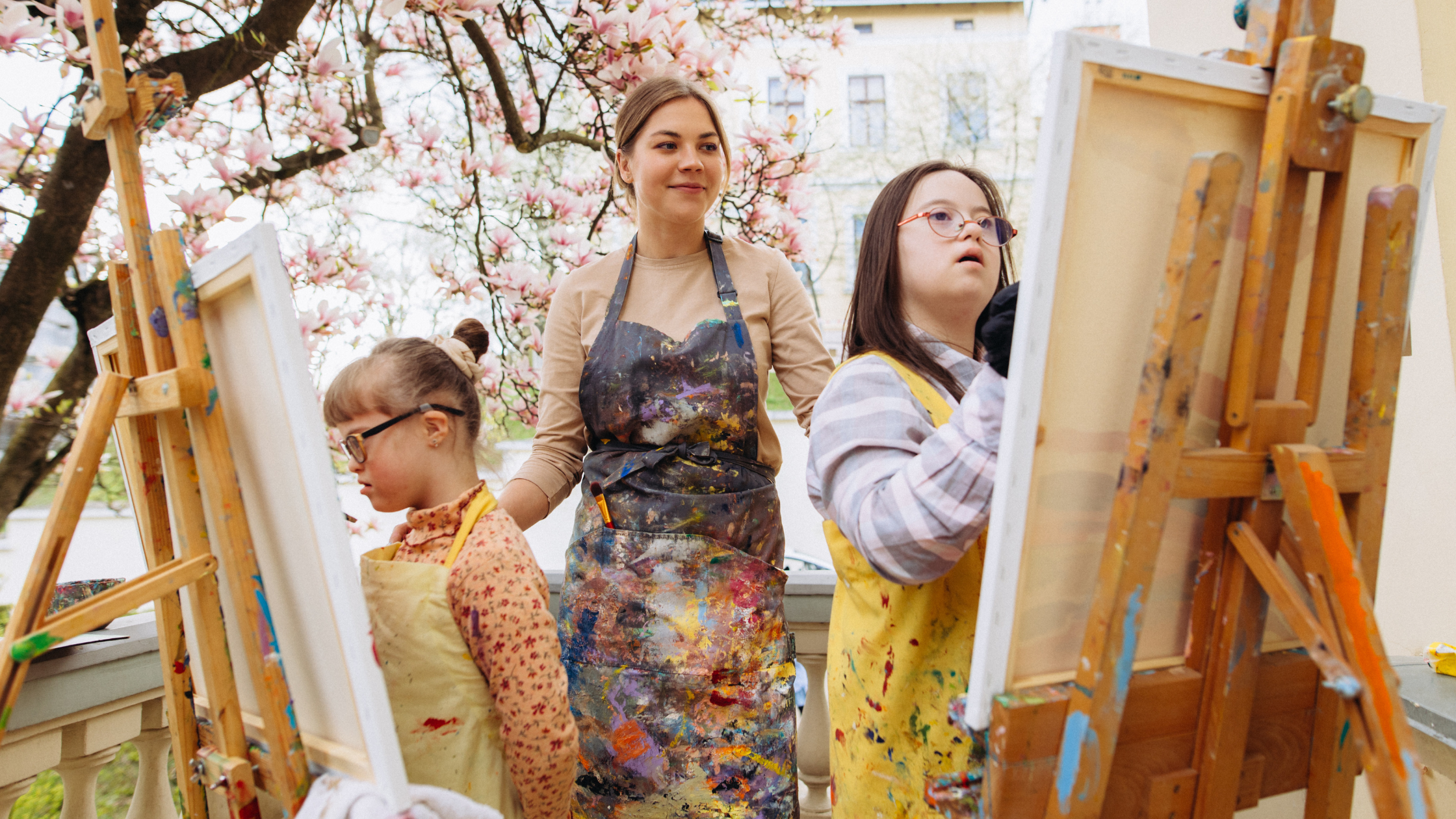 Young lady helping two girls with special abilities to paint on a canvas